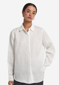 Camicia bianca in lino con colletto classico, maniche lunghe e vestibilità rilassata, caratterizzata da una trama sottile e chiusura frontale con bottoni.