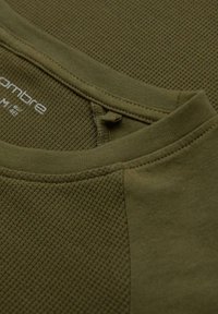 Olivgrünes, strukturiertes Strickshirt mit Rundhalsausschnitt und kontrastierenden glatten Ärmeln. Der Stoff hat ein leichtes, atmungsaktives Gefühl.
