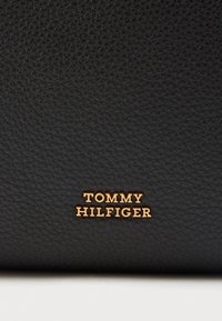 Černá strukturovaná kožená peněženka s vyraženým názvem značky "TOMMY HILFIGER" v zlatém písmu ve spodní části.
