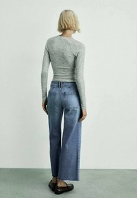 Camisa de manga larga gris, jeans de pierna ancha azul claro con dobladillo sin rematar y mocasines negros. Textura de tela suave y diseño de ajuste relajado.