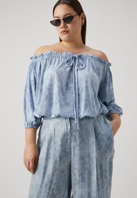 Top de culoare albastru deschis, cu umerii descoperiți, având un model texturat, decolteu elastic și șnur de ajustare. Asortat cu pantaloni largi, de aceeași culoare.