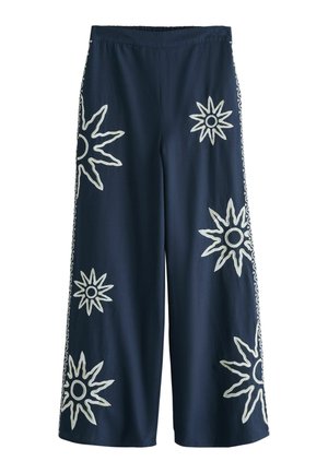 Navy wide-leg pants with white embroidered sun designs scattered on front and sides, elastic waistband, mid-length cut.