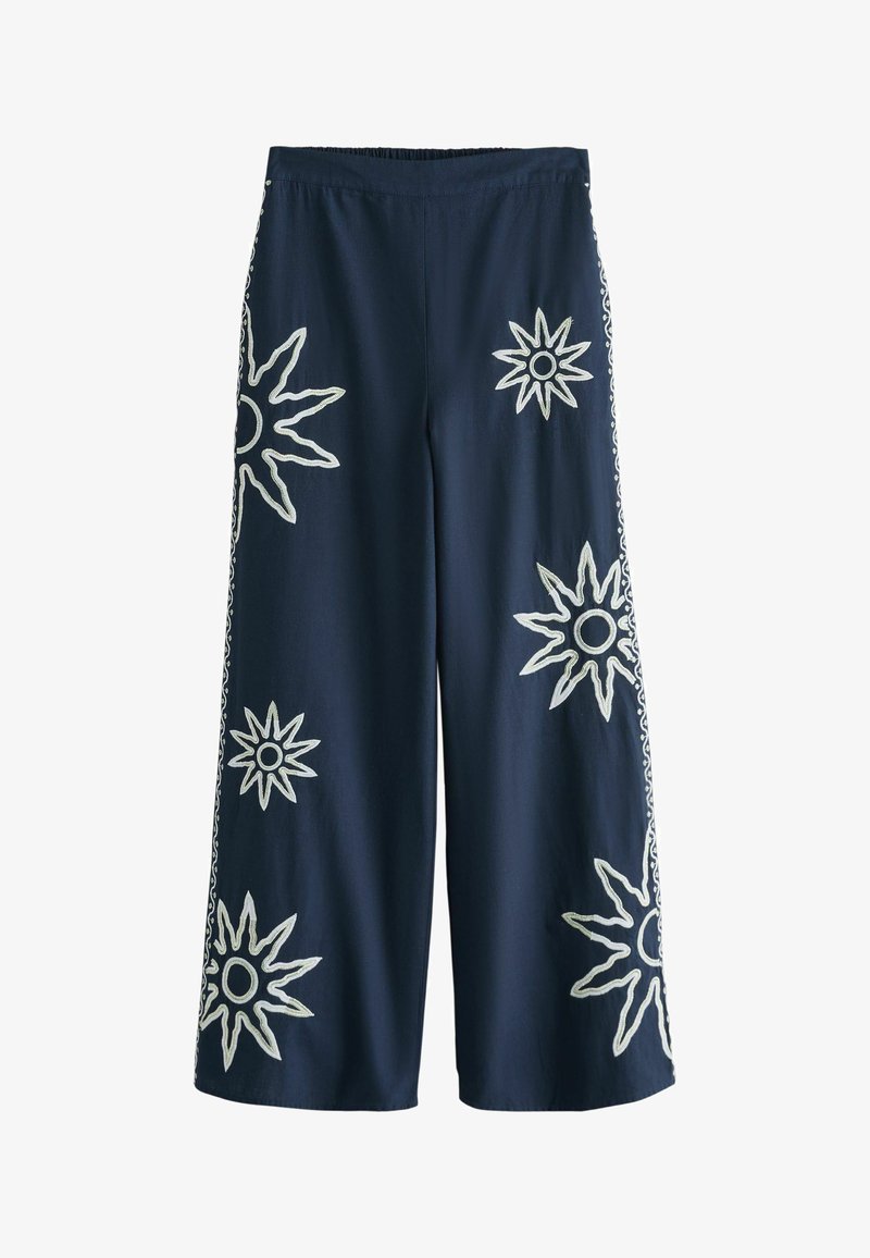 Pantalon large marine avec motifs de soleil brodés en blanc dispersés à l'avant et sur les côtés, taille élastique, coupe mi-longue.