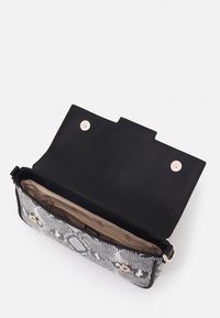 Bolso de mano con estampado de serpiente en negro y gris, con una textura suave, herrajes de plata y cierre a presión magnético; se abre a un interior beige con bolsillos.