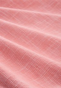 Tessuto di colore corallo con un motivo a griglia testurizzato. Il tessuto ha un aspetto morbido, mettendo in evidenza pieghe delicate e drappeggi.