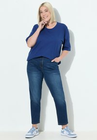 Camiseta azul de manga corta con escote redondo, combinada con jeans rectos de lavado medio y zapatillas deportivas azul claro. Look simple y casual.