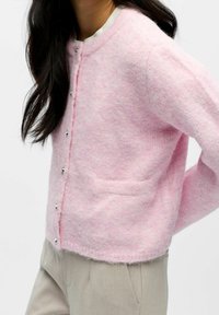 Rozā džemperis, kas izgatavots no mīksta, strukturēta auduma, ar apaļu dekoltē, garām piedurknēm un sudraba pogām priekšpusē.