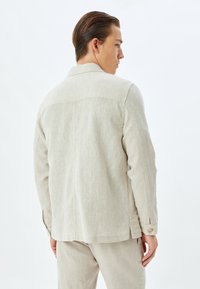 Lichtbeige linnen jack met een relaxte pasvorm, lange mouwen, rugplooien en knoopmanchetten; voorzien van een gestructureerde, geweven stof.