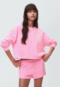 Rosa kortärmad sweatshirt och matchande shorts i mjuk bomullsblandning. Har avslappnad passform, ribbade muddar och dragsko i midjan.