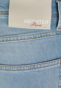 Light blue denim fabric with a back pocket and a beige label featuring "HECHTER" in white and "Paris" in red cursive text.