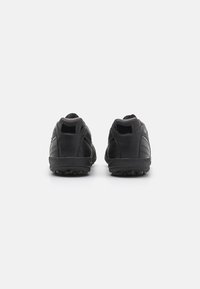 Schwarze Sportschuhe mit einem glatten synthetischen Obermaterial, runder Zehenpartie und strukturierten Sohlen, die mit mehreren kleinen Noppen für bessere Traktion versehen sind.