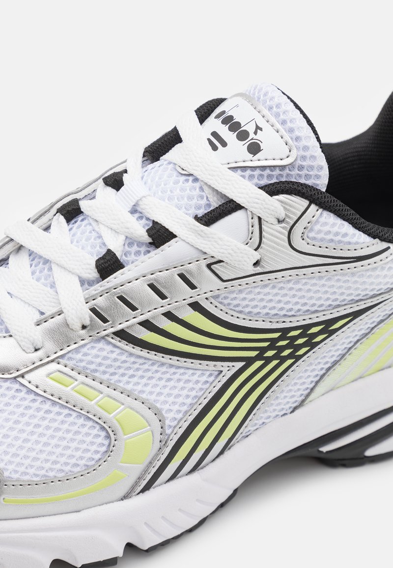 Witte sportieve schoen met mesh bovenwerk, zwarte en zilveren accenten en limegroene details. Beschikt over een ronde neus en een gestructureerde rubberen zool.