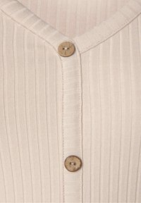 Vaaleanbeige uritettu kangas, jossa on V-pääntie ja puinen nappi keskellä edessä. Kangas on pehmeä ja hieman venyvä.