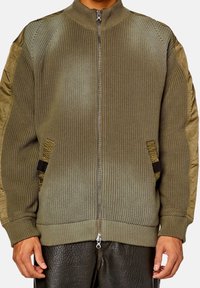 Olivgrön bomberjacka med ribbad stickad kropp, släta ärmar i tyg, dragkedjestängning och sidofickor. Har strukturerad detaljering på axlarna.