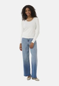 Vit långärmad tröja med spetsdetaljer, i kombination med ljusblå vida jeans och beige skor. Enkel och avslappnad outfitdesign.