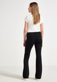 Zwarte flared trousers met een gladde textuur, voorzien van een middelhoge tailleband en achterzakken, gecombineerd met een witte top met korte mouwen.