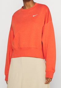 Rot-orange, verkürzter Sweatshirt aus weichem Stoff. Mit geripptem Kragen und Bündchen, auf der Brust befindet sich das weiße Nike-Logo.