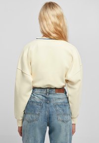 Light yellow, oversized sweatshirt with dropped shoulders, paired with high-waisted blue denim jeans featuring a leather patch and faded texture.