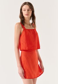 Completo a due pezzi di un vivace rosso, composto da un canottiera con bordi scallop e una gonna svasata. Realizzato in un tessuto leggero e strutturato.