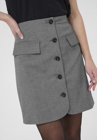 Jupe gris à rayures avec fermeture à boutons à l'avant, deux poches plaquées et une légère forme évasée. Fabriquée à partir d'un tissu structuré, longueur au-dessus du genou.