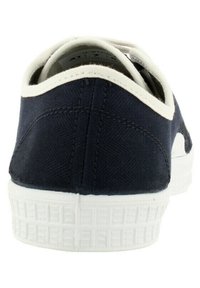 Zapatilla de lona azul marino con parte superior texturizada, suela de goma blanca y tab de talón blanco en contraste; presenta costuras mínimas y un diseño de perfil bajo.