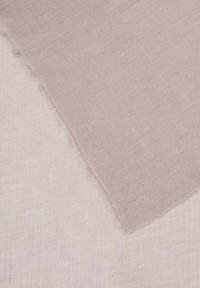 Lichtgewicht stof in zacht beige, gedeeltelijk gedrapeerd over een vergelijkbaar lichtgekleurde materiaal. Randen zijn rauw en rafelig, wat een textuurcontrast laat zien.