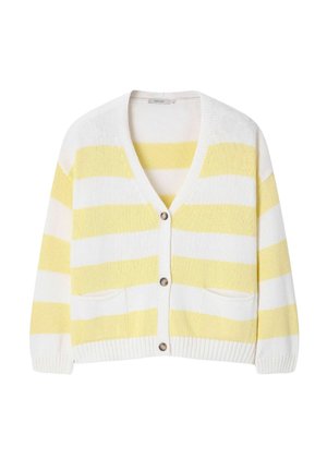 Femme portant un cardigan rayé jaune et blanc, un short blanc, une casquette beige et des chaussures, tenant un grand sac fourre-tout jaune avec un texte vert.