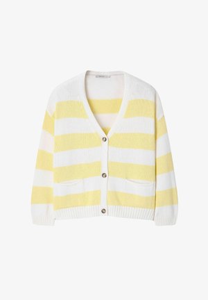 Femme portant un cardigan rayé jaune et blanc, un short blanc, une casquette beige et des chaussures, tenant un grand sac fourre-tout jaune avec un texte vert.