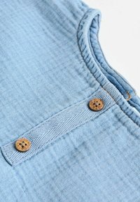 Helles blaues Baumwollgewebe mit einer strukturierten Oberfläche, ausgestattet mit einem Knopfverschluss und kontrastierenden Nähten entlang des Halsausschnitts und der Knopfleiste.