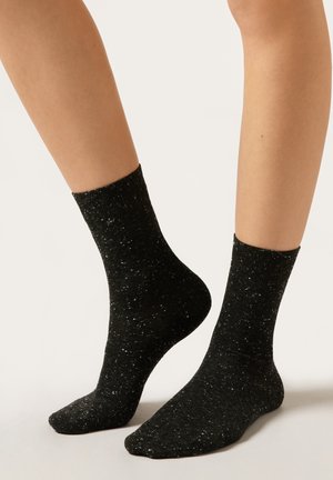 Schwarze Socken mit einem gesprenkelten Design, versehen mit einer weichen Textur und einer mittleren Wadenhöhe. Leichter Stoff mit dezenten schimmernden Akzenten.