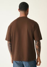 Brun kortærmet t-shirt lavet af blødt stof, med en afslappet pasform og enkelt design, med syede detaljer langs kanten.