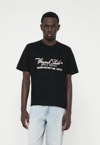 Musthave musta puuvillane T-särk lühikeste varrukatega, millel on valge ja kuldne graafiline tekst. Kanti helesiniste denim-jaaride juurde.