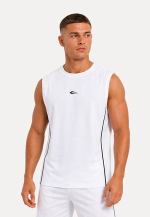 Homme musclé portant un maillot de sport blanc sans manches avec des lignes latérales noires et un petit logo noir sur la poitrine, regardant sur le côté.