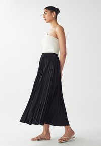 Black pleated maxi skirt with an elastic waistband, paired with a fitted white ribbed tank top and nude strappy sandals.