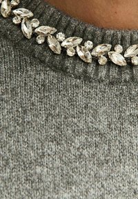 Grijze gebreide trui met een textuurafwerking, voorzien van een kraag versierd met heldere, facetten geslepen edelstenen in verschillende vormen.