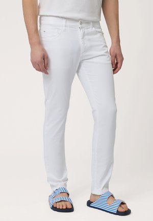 Witte katoenen broek met een slim fit, voorzien van een rits en voorkeuringen. Gecombineerd met blauw-witte gestreepte schuifslippers.