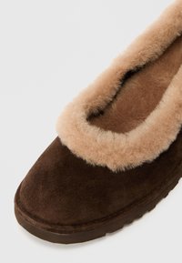 Pruun nahast slippertel on pehme, helepruun karvane krae. Tallal on lame pinnas, millel on tekstureeritud haardevuus stabiilsuse jaoks.