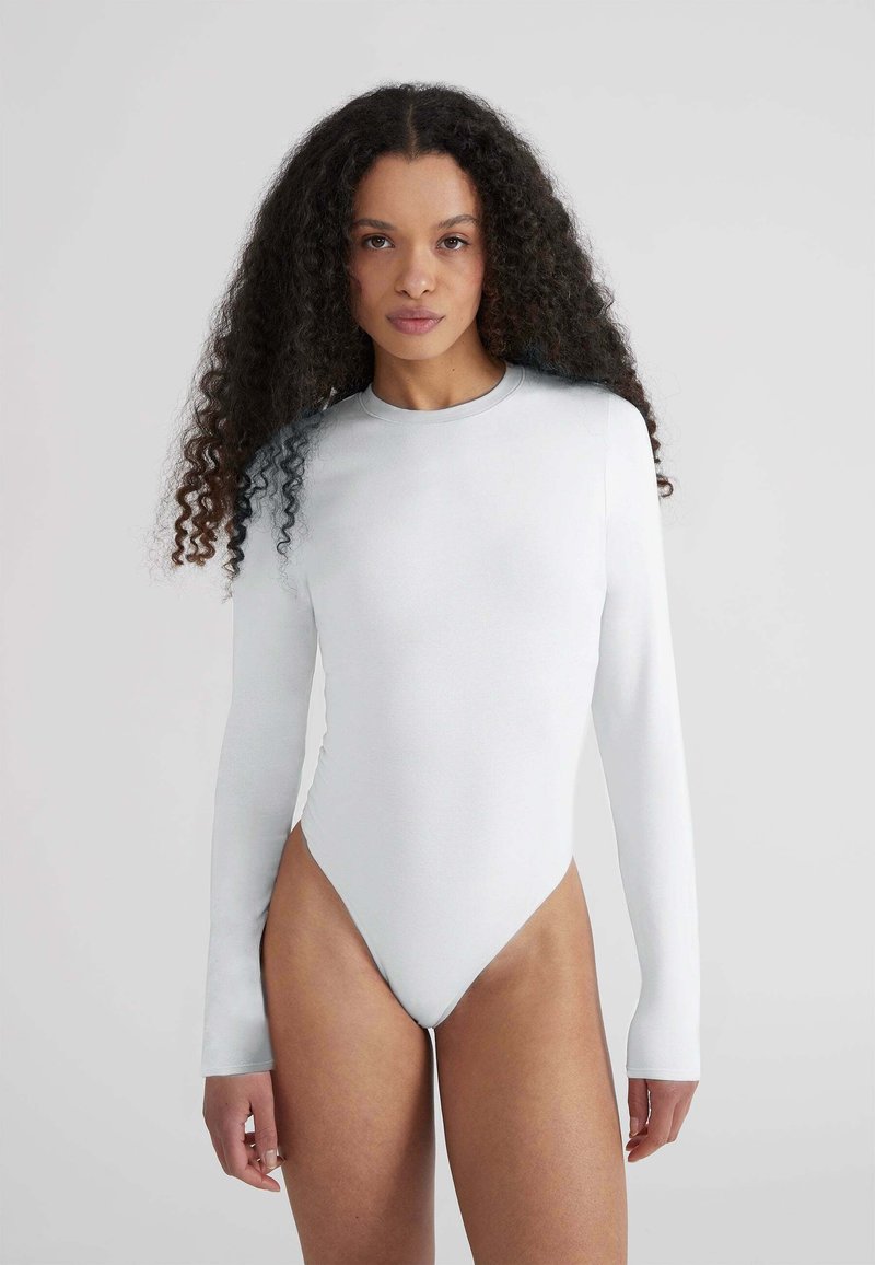 Body a maniche lunghe in morbido tessuto bianco, con scollatura tonda e aperture audio alte, dal design aderente.
