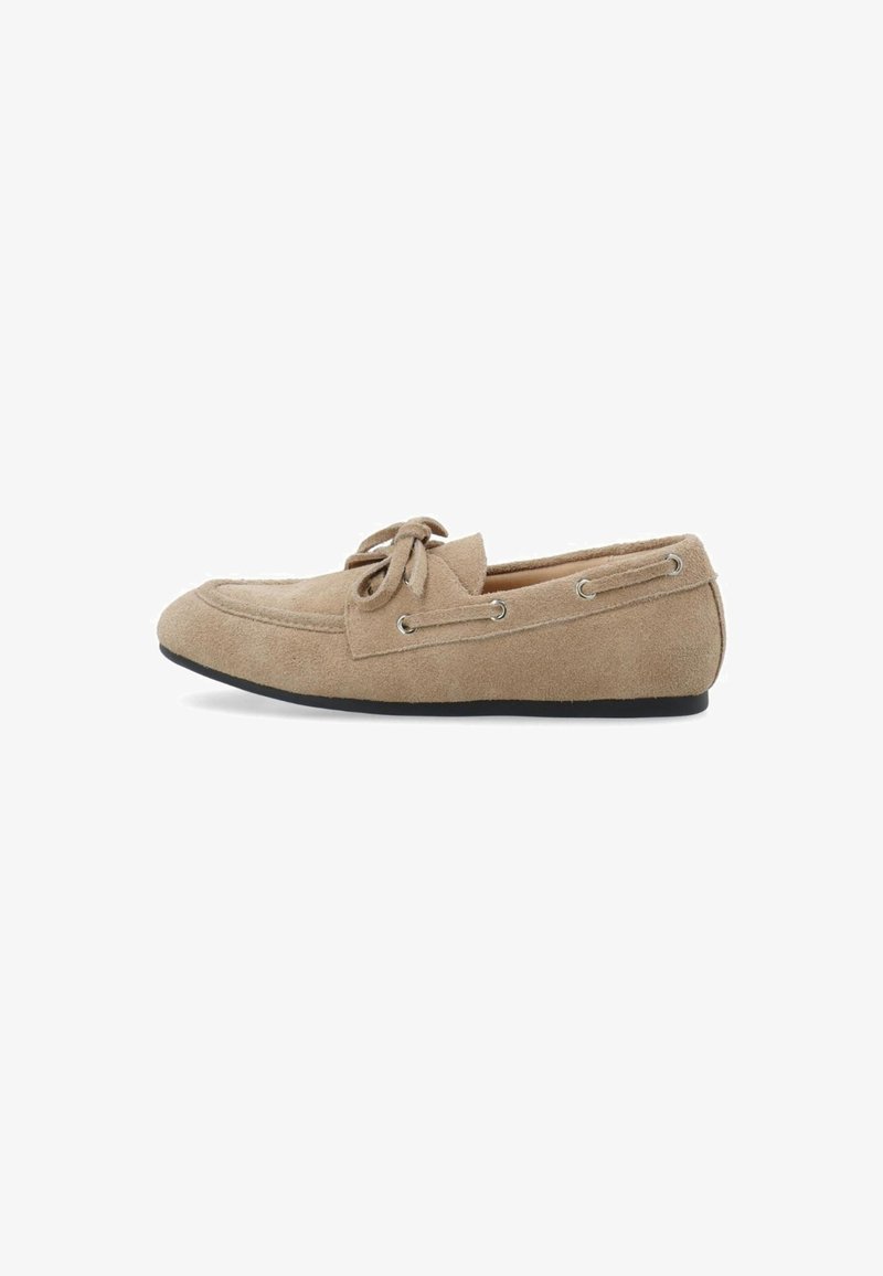 Beige suede moccasin shoe with a rounded toe, lace-up detail, and silver eyelets, featuring a flat black rubber sole.