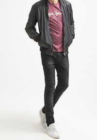 Schwarze Leder-Bomberjacke, bordeauxfarbenes T-Shirt mit Logo, schwarze, eng geschnittene Jeans und weiße Sneaker. Einfaches Design, glatte Textur, moderner Look.