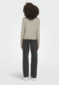 Pull gris clair en maille avec une taille cintrée, assorti à un jean denim noir à coupe ample. La tenue est complétée par des baskets blanches.