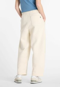 Pantalons de jogging larges de couleur crème avec une taille élastique, poches latérales et une poche arrière. Portés avec des baskets de couleur claire.