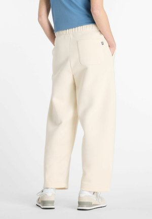 Crème-kleurige, wijdvallende sweatpants met een elastische tailleband, zijzakken en een achterzak. Draagt met lichtgekleurde sneakers.