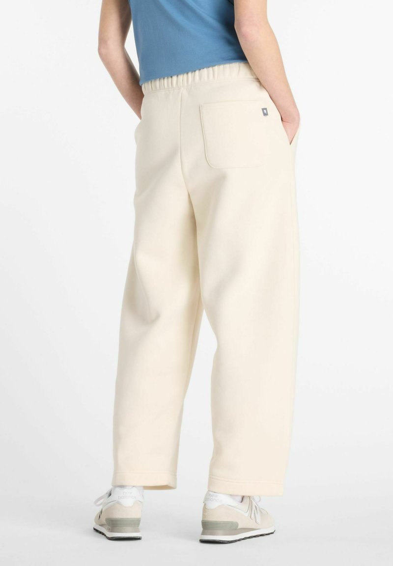 Pantalons de jogging larges de couleur crème avec une taille élastique, poches latérales et une poche arrière. Portés avec des baskets de couleur claire.