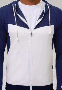 Giacca con cappuccio e zip in blu navy e bianco con design a blocchi di colore. Realizzata in tessuto liscio con zip frontale e coulisse regolabili.
