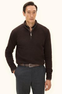 Brauner Zip-Pullover aus weichem Material, kombiniert mit grauen Hosen und einem braunen Gürtel. Hat ein schlichtes Design und eine taillierte Silhouette.