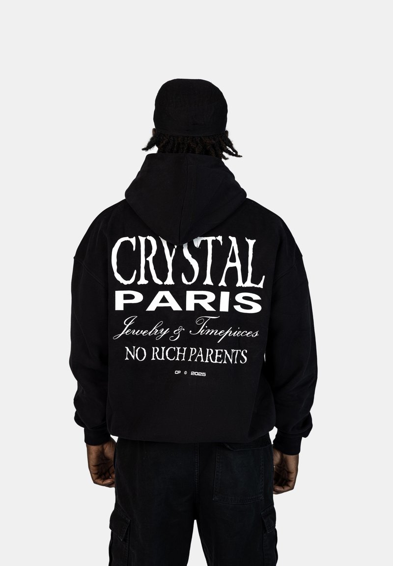 Felpa nera con grande testo bianco sul retro: "CRYSTAL PARIS Gioielli & Orologi NESSUN GENITORE RICCO." Il materiale sembra morbido.