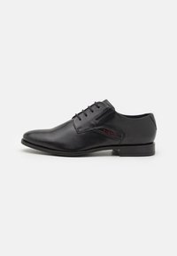Chaussure habillée en cuir noir avec un bout rond, un design à lacets et un logo discret en rouge. Texture lisse et talon bas.