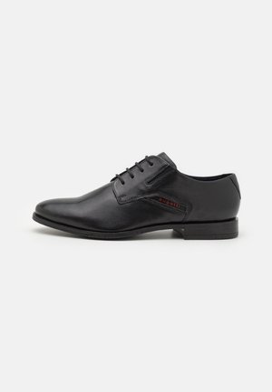 Chaussure habillée en cuir noir avec un bout rond, un design à lacets et un logo discret en rouge. Texture lisse et talon bas.