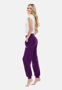 Pantaloni da jogging viola con polsini elastici e tasche laterali, abbinati a una maglietta aderente bianca a maniche corte, esposti su uno sfondo neutro.